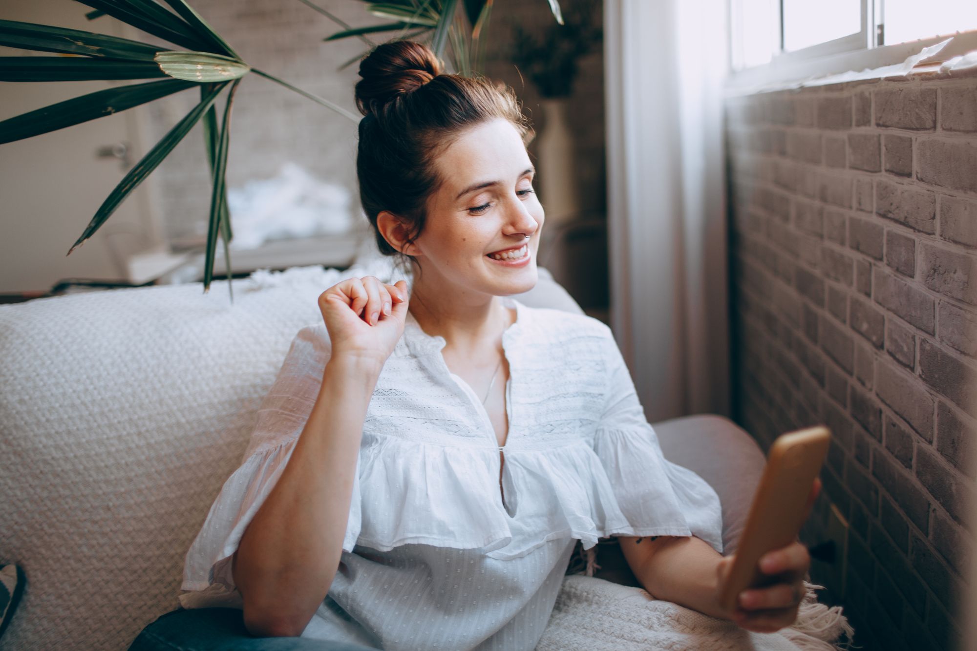 Woman smiling at her phone on a sofa at home